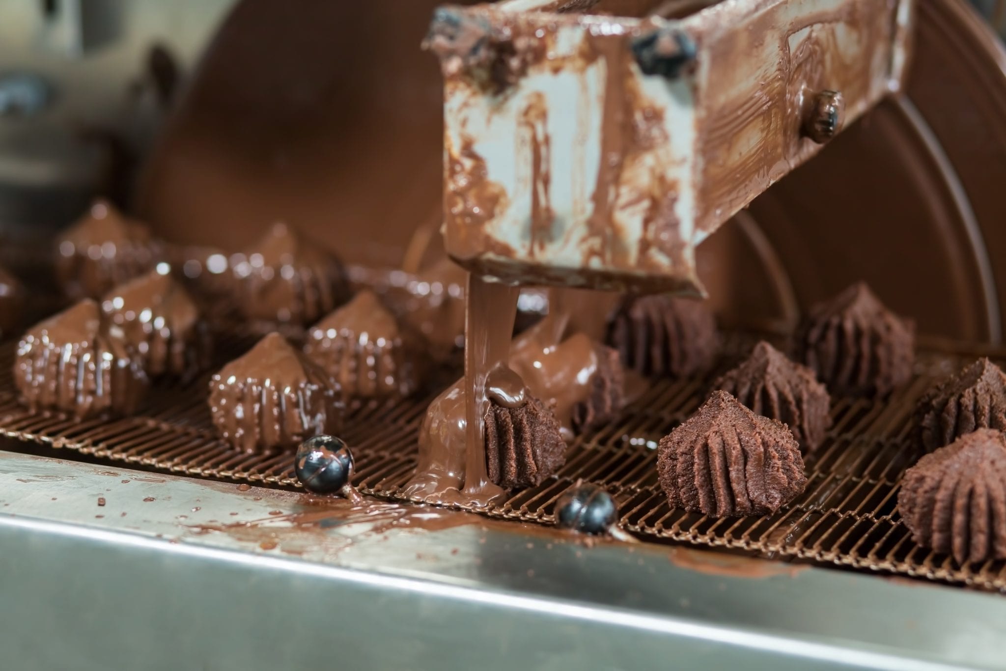 Conveyor pouring liquid onto sweets. Dark candies on conveyor line. Dessert produced at local plant. Chocolate glaze for tasty candies.