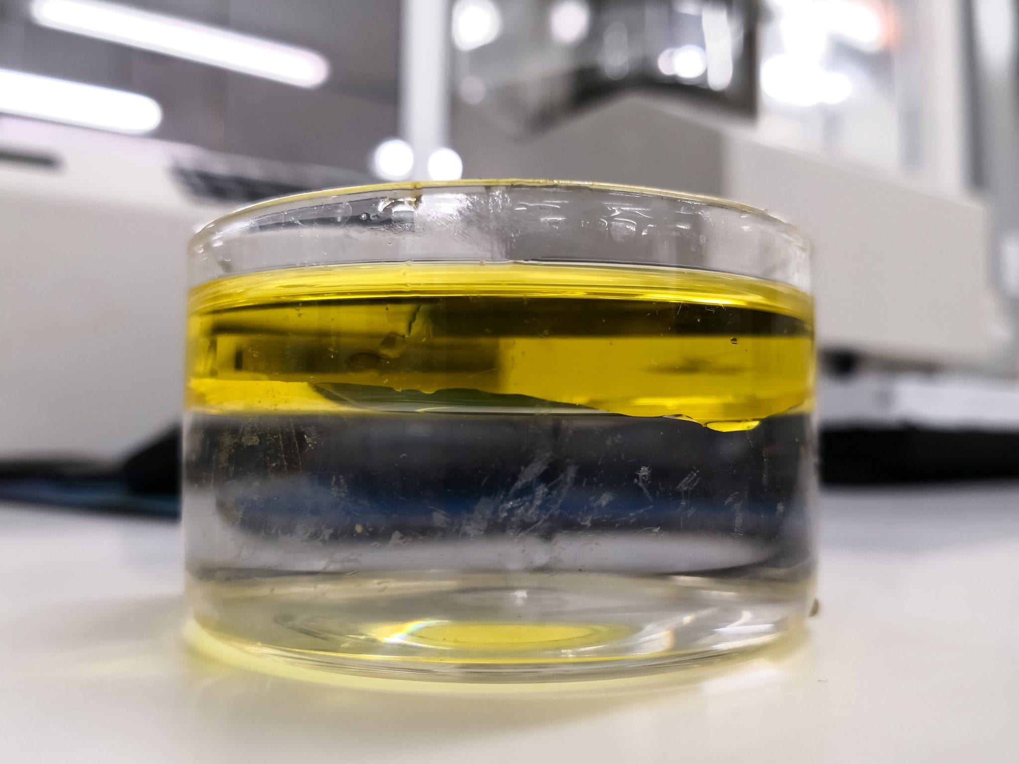 Interface between water and oil, two immiscible liquids, inside a glass beaker in a scientific laboratory